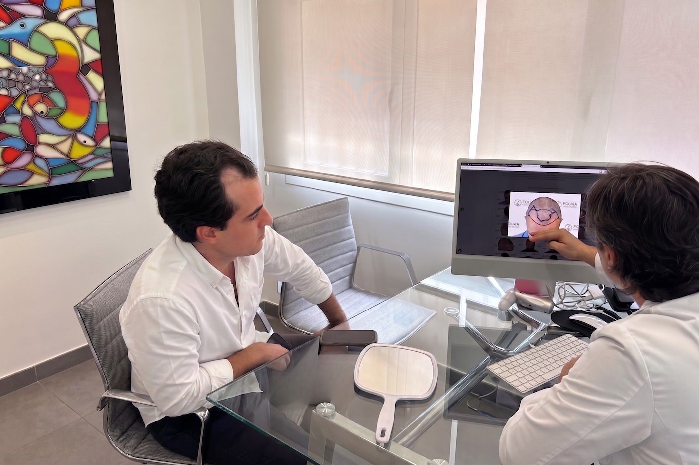 Doctor de Folika Hair Clinic mostrando a un paciente joven el diseño de su línea frontal en el ordenador durante una primera consulta para valorar un injerto capilar a edad temprana.