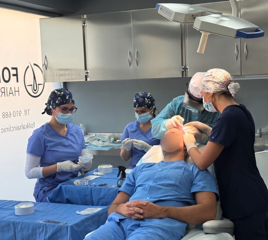 Cirujano y equipo de enfermeras de Folika Hair Clinic trabajando coordinadamente en la implantación de folículos en la primera línea de un paciente en su clínica de Madrid.