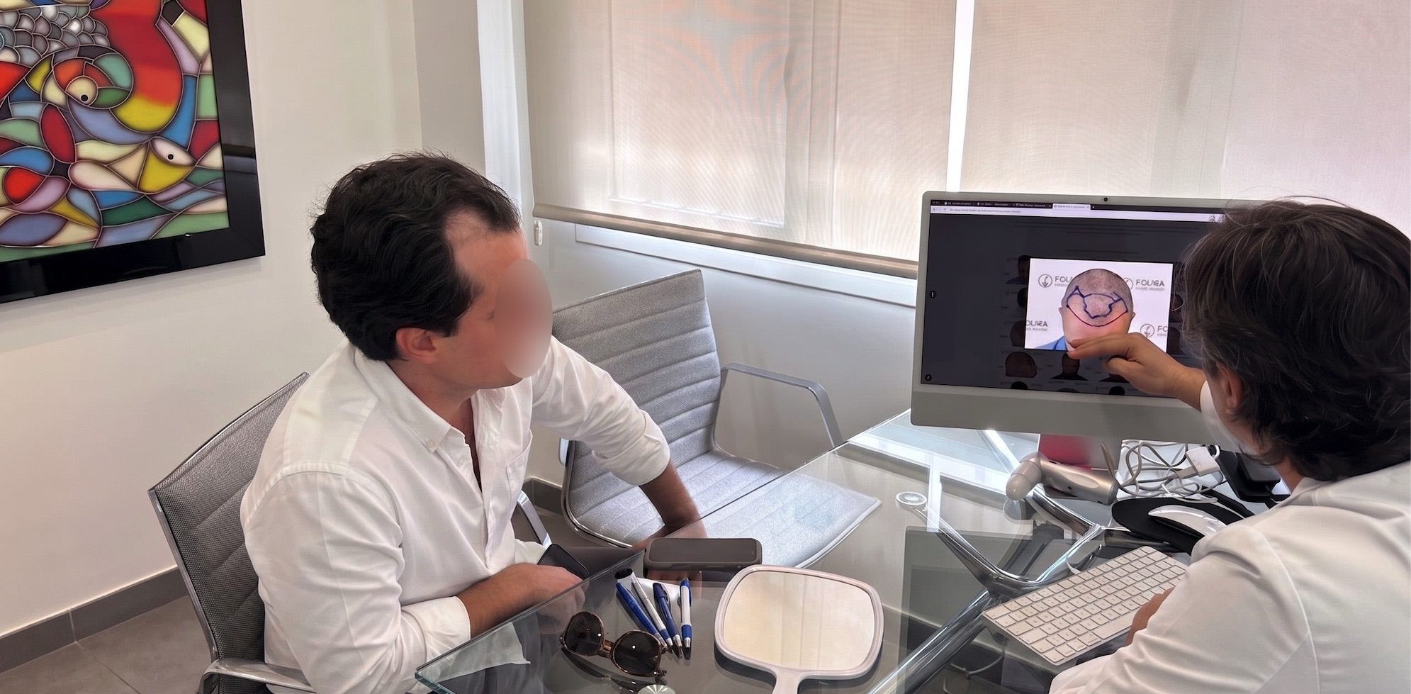 Médico especialista de Folika Hair Clinic mostrando el diseño de un injerto capilar a un paciente en la pantalla del ordenador durante su primera consulta en Madrid.